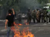 Imagen de un protestante iraní enfrentándose a la Policía delante de unos escombros en llamas.