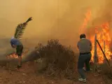 Dos voluntarios intentan apagar las llamas en Dioni, a 12 kilómetros al norte de Atenas