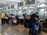 Pasajeros con sus equipajes esperan junto a mostradores del aeropuerto de El Prat de Llobregat (Barcelona).