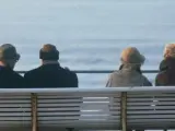 Varios jubilados sentados en un paseo marítimo.