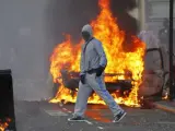 Un hombre encapuchado cruza una calle cortada por contenedores ardiendo en el conflictivo barrio de Hackney de Londres.