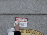 Una persona coloca una pegatina a favor de la huelga general en la fachada del Ministerio de Empleo.
