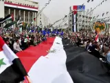 Fotografía cedida por la Agencia de Noticias siria, SANA, que muestra a decenas de personas portando una bandera nacional siria durante una manifestación celebrada para conmemorar el 65 aniversario de la fundación del Partido Socialista Árabe en la Plaza Sabe Bahrat en Damasco, Siria.
