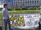 Dos jóvenes en la Plaza de Cataluña sostienen una pancarta con un 12-M escrito en ella, el día de inicio oficial de los actos conmemorativos del aniversario del movimiento 15-M.