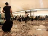 Viajeros circulan por la zona de salidas de la T1 en el aeropuerto del Prat, lleno de basura.