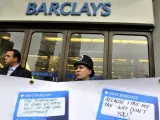 Un policía británico y un guardia de seguridad vigilan tras una pancarta donde los manifestantes pegan mensajes frente a una sucursal de Barclays.