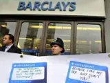 Un policía británico y un guardia de seguridad vigilan tras una pancarta donde manifestantes han pegado mensajes de protesta frente a una sucursal de Barclays en Londres, durante una manifestación contra el exconsejero delegado de la entidad, Bob Diamond.