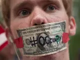 Un manifestante de 'Occupy Wall Street' se tapa la boca con un billete de dólar en el parque Zuccotti de Nueva York, donde hace un año surgió el movimiento.
