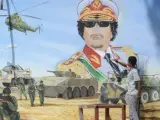 Un joven utiliza un objeto punzante para destruir una pintura mural que representa al líder libio, Muamar el Gadafi.
