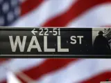Imagen de un cartel de Wall Street con la bandera estadounidense de fondo.