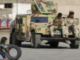 Una niña juega con un neumático mientras dos soldados descansan en su vehículo militar en Bagdad.
