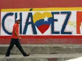 Un hombre camina frente a una pared pintada con referencia al presidente venezolano, Hugo Chávez.
