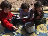 Unos niños sirios comen en el suelo en un campamento de refugiados.