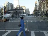 Una mujer cruza una calle junto a la meta de la maratón de Boston, mientras continúan las investigaciones en el escenario de las dos explosiones.