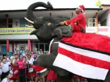 Un elefante manejado por un "mahout" (entrenador) y vestido como Santa Claus entrega regalos a los niños en una escuela de Ayutthaya (Tailandia). El evento se celebra cada año en esta provincia para celebrar la llegada de Navidad y promover el turismo.