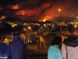 Cuatro personas observan cómo un incendio forestal arrasa con zonas urbanas en la ciudad de Valparaíso, Chile.