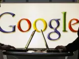 Dos personas navegan con su portátil con el logotipo de Google al fondo.