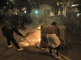Dos jóvenes colocan un contenedor incendiado como barricada durante los incidentes tras la marcha hacia la comisaría de los Mossos d'Escuadra de Les Corts, en Barcelona.