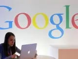 Una usuaria consulta su ordenador frente a un logo de la compañía Google.