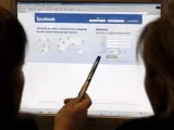 Dos personas observan la página de inicio de Facebook.
