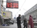 Dos transeúntes hablan ante un panel que muestra el cambio de divisas en Moscú.