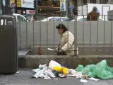 Una mujer sale del metro hacia una calle llena de basura y desperdicios.