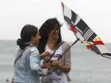 El viento impide a unas jóvenes protegerse con un paraguas de la lluvia, en la playa de la Zurriola de San Sebastián.