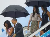 Obama y su familia descienden del avión presidencial Air Force One con paraguas.