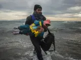 Un refugiado lleva en brazos a un beb&eacute; al bajar de una embarcaci&oacute;n junto a m&aacute;s refugiados y migrantes en la isla griega de Lesbos.
