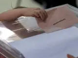 Una ni&ntilde;a intenta meter por s&iacute; misma el sobre en la urna con el voto de su madre para el Senado, este mediod&iacute;a en un colegio electoral del barrio de Triana en Sevilla.