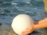 Una mujer deposita en el mar una urna funeraria hecha con sal.
