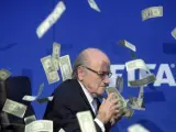 El presidente de la FIFA, Joseph Blatter, bajo una lluvia de billetes que le lanzó el humorista británico Simon Brodkin, durante una rueda de prensa para presentar los resultados de la reunión del Comité Ejecutivo de la FIFA en su sede de Zúrich, Suiza.