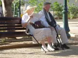 Dos ancianos descansan en un banco de un paseo.
