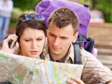 Dos turistas llaman por tel&eacute;fono mientras consultan un mapa.