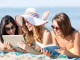 Turistas en una playa leyendo un libro y consultando una tablet.