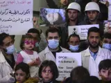 Niños sirios, voluntarios y personal de servicios de primeros auxilios muestran pancartas e imágenes de las víctimas de un supuesto ataque químico durante una concentración en Douma, Siria.