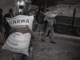 Palestinos cargan con sacos de harina en un centro de distribución de la Agencia de las Naciones Unidas para los Refugiados Palestinos (UNRWA), en el campo de refugiados de Al Shati, al norte de Gaza.
