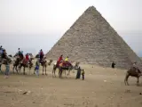 Varios turistas disfrutan de un paseo a camello delante de la Pirámides en Guiza (Egipto).