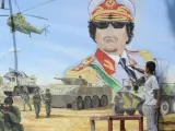 Un joven utiliza un objeto punzante para destruir una pintura mural que representa al dictador libio Muamar el Gadafi, muerto en octubre de 2011.