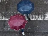 Dos peatones cruzan por un paso de cebra, tapándose de la lluvia con su paraguas, en la ciudad gallega de Ourense.