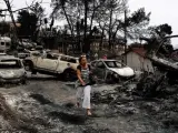 Una mujer camina entre coches calcinados en Mati (Grecia), localidad arrasada por los devastadores incendios declarados en la costa al noreste de Atenas.