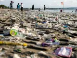 Varias personas caminan por la playa sobre una alfombra de restos de plástico usado que llegaron a la costa traídos por fuertes olas en la playa de Kuta, en Bali (Indonesia).