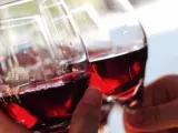 Un grupo de personas brindan con copas de vino tinto.