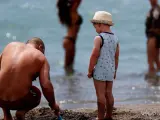 Un hombre juega con la arena junto a un ni&ntilde;o y otras personas que disfrutan del buen tiempo en la playa del Bajondillo en Torremolinos ( M&aacute;laga).