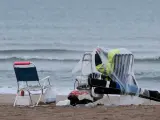Una persona se protege de la lluvia con un plástico en la playa de la Malvarrosa.