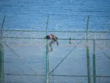 Imagen de archivo de un migrante saltando la doble valla de Ceuta.
