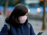 Una mujer asiática mira su móvil con una mascarilla protectora, mientras las farmacias registran una alta demanda de estas por parte de ciudadanos chinos tras el coronavirus, en Madrid (España), a 30 de enero.