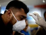 Un viajero con mascarilla pasa un control de temperatura en El Salvador