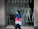 Una mujer protegida con una mascarilla pasa junto a un escaparate de una tienda cerrada en Barcelona durante el estado de alarma por el coronavirus.