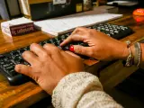 Unas manos de mujer escriben en el teclado de un ordenador, sobre una mesa de madera.